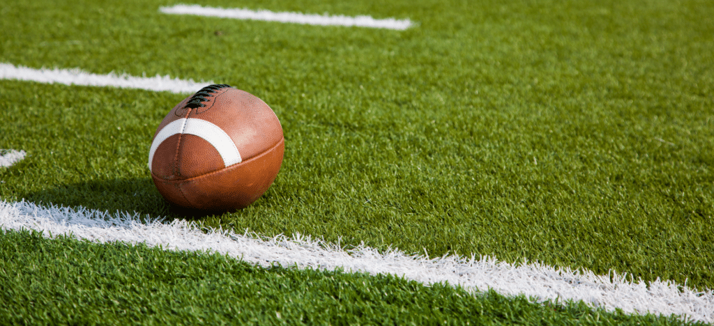 A football resting on a green field with white yard lines, symbolizing the sport and its equipment.